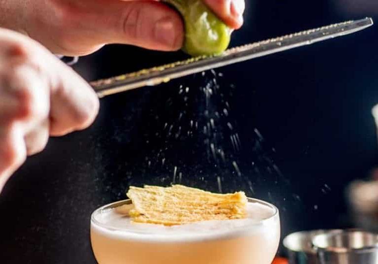 barman rubs lime zest on cocktail. bartender is preparing a cocktail for serving.Finishing a Cocktail. Mixology